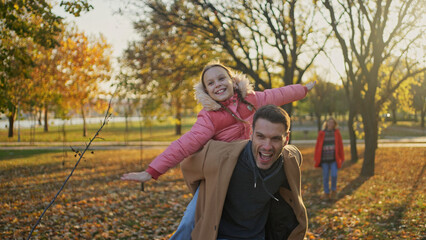 Father giving daughter a piggyback ride in a sunny autumn park