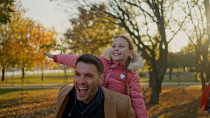 Fototapeta premium Father giving his daughter a piggyback ride in a park on a sunny autumn day