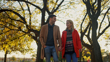 Couple walking hand-in-hand in a park during autumn, enjoying a sunny day