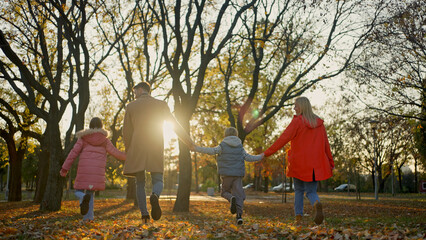 Family enjoying a sunny autumn day in a park, holding hands and running together