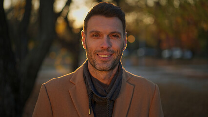Handsome man smiles at camera in a park during golden hour