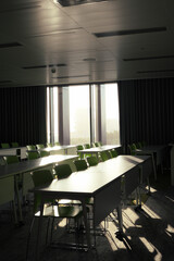 Empty Modern Classroom with Green Chairs and Desks Lit by Morning Sunlight Through Large Windows