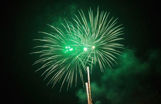 Spectacular green fireworks display against dark sky. Bright bursts explode showcasing festive celebration. Beautiful pyrotechnics illuminate night. Perfect background for holiday greeting cards.