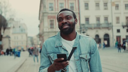 Young african amerian man goes down the street and uses the phone look around happy smile internet face technology fashion black call texting attractive smartphone communication handsome message