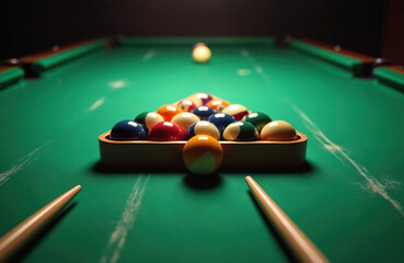 Pool balls in triangle rack on green felt table. Two cues rest on felt beside triangle. One ball sits in front of rack. Focus on game setup.
