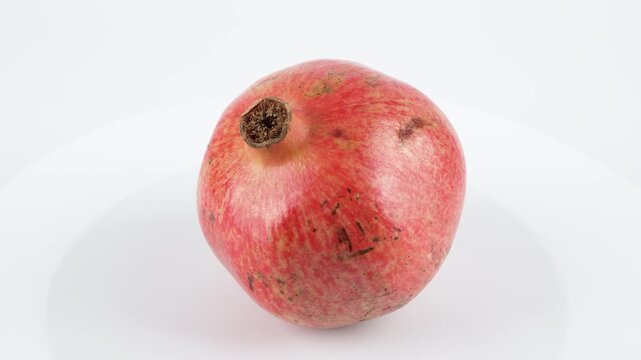 Pomegranate Isolated. A single ripe pomegranate rotates on a white surface. The vivid red skin and subtle imperfections give a realistic, natural appearance.