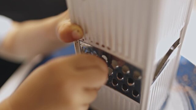 Child's hands grating nutmeg spice on a kitchen grater
