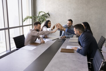 Multicultural businesspeople unite hands making high five above boardroom table