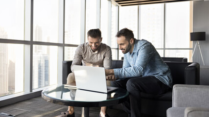 Two happy young business professionals review presentation on notebook screen