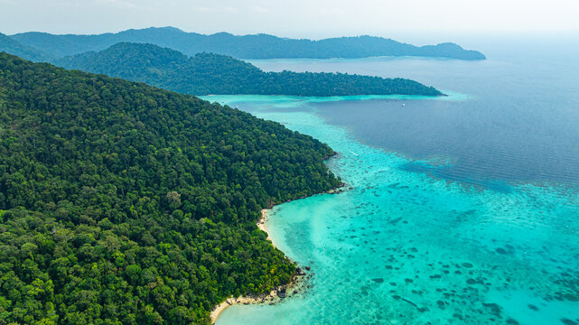 A breathtaking aerial view of a secluded Surin islands with crystal-clear turquoise waters, surrounded by lush green vegetation and corel reef. The pristine white sand and vibrant ocean hues