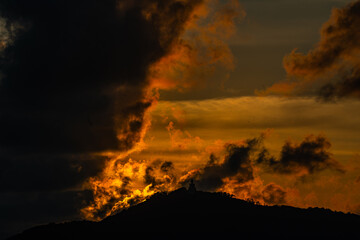 The golden sun sets behind the mountain casting a warm glow around the grand Big Buddha of Phuket. Silhouetted against a radiant sky, the sacred statue radiates peace and spiritual serenity.