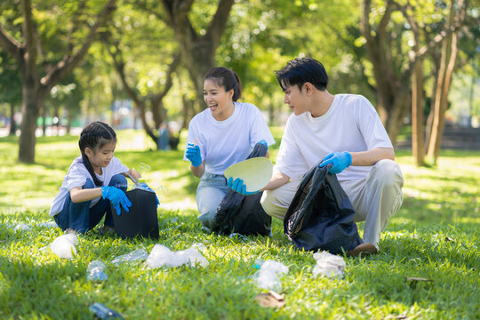 Asian family collects plastic bottles into black bags at a park on the weekend. - Powered by Adobe