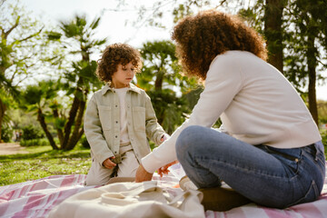 The son is sitting on a blanket next to his mother, who is holding her hand near the tray