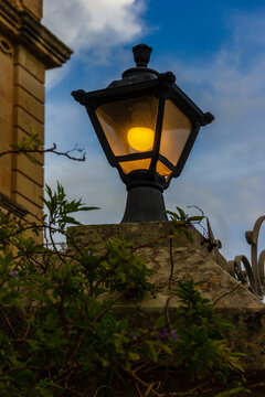 Vintage Streetlamp With Warm Glow Over Stone Wall Amid Ivy And Evening Sky