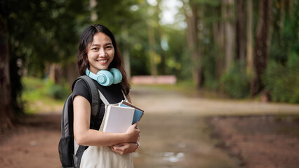 Smiling college student with books and headphones on campus path