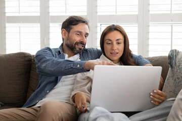 Happy married couple cuddle on couch using notebook together