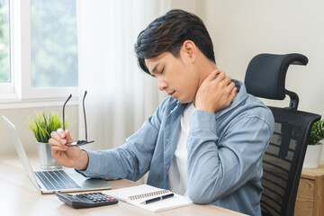 Body muscles stiff problem, ache asian young man pain neck and shoulder while sitting work on chair...