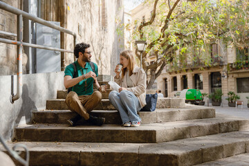 A woman drinks from a cup and listens to a man sitting next to her on the stairs