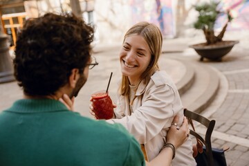 A woman smiles and holds a cup while placing her hand on the neck of a man who has placed his hand on her waist