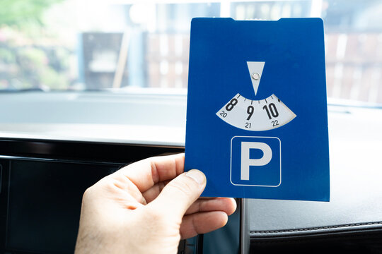 Close up hand hold blue parking disc in the car. Parking time restrictions in busy parking lots. Limited time duration park place zone.