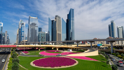 Beautiful decorative road junction with lawns, flower beds with pink petunias and palm trees in city Dubai, United Arab Emirates. The road ring. Ring traffic. Skyscrapers and high-rise buildings