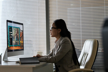Side view of young female Asian manager sitting in modern office at computer and having video chat...