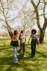 Fototapeta premium A group of three female friends are walking on the grass and laughing while talking