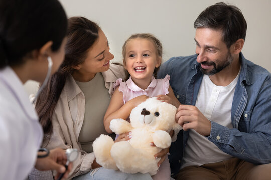 Smiling preschool girl sitting on couch chatting with friendly doctor