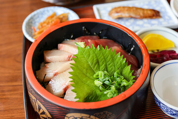 黒い漆塗りの器に大葉と刻みネギが盛り付けられた海鮮丼