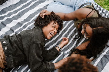 Obraz premium A woman puts her hand on the head of her female friend while they laugh and lie on a blanket