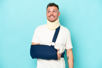 Young caucasian man wearing a sling  and neck lace isolated on blue background thinking an idea...
