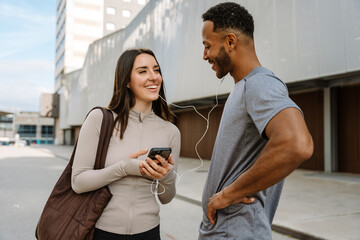 Male and female athletes are talking and smiling while listening in earphones and she is holding the phone