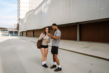 A male athlete looks at the phone he is holding while standing next to a female athlete while they...