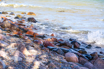 Rocky pebble beach with waves washing over colourful stones. Ocean surf breaking on shoreline covered with smooth, rounded rocks and pebbles.