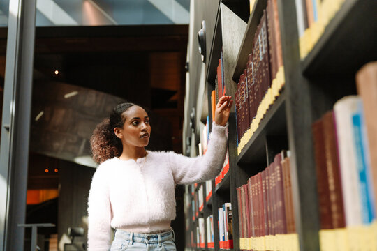 A female student stands and chooses a book on the bookshelf next to which she holds her hand