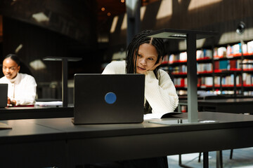 A female student looks at a laptop and sits at a table while resting her head on her hand