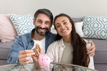 Happy millennial husband wife prepare to drop coins to piggybank