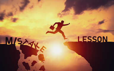Silhouette of businessman jumping over cliff from word Mistake to Lesson. Concept of determination and learning from mistakes to create opportunities to overcome and grow in future business path. © Midnight Studio