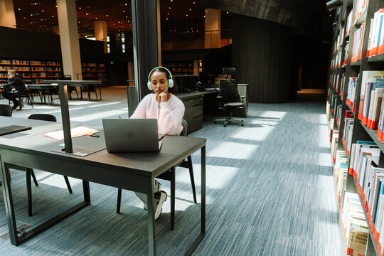 A female student is concentrating on a laptop and sitting at a table while listening in headphones