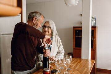 A woman listens to a man standing next to her at the table and opens a bottle