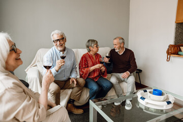 A group of four friends are holding glasses and talking in pairs while sitting on the couch
