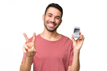 Young handsome caucasian man holding a engagement ring over isolated background smiling and showing victory sign