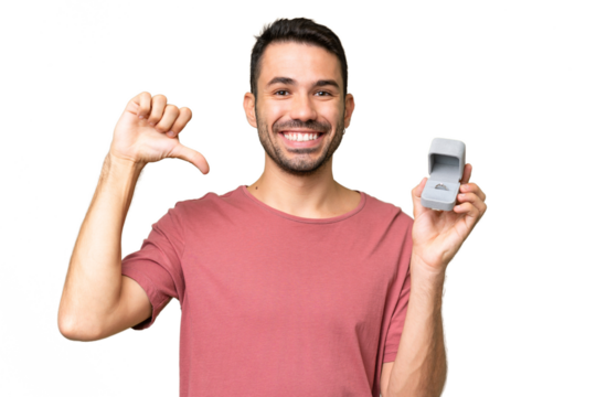 Young handsome caucasian man holding a engagement ring over isolated background proud and self-satisfied