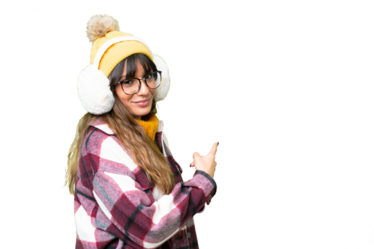 Young caucasian woman wearing winter muffs over isolated chroma key background pointing back