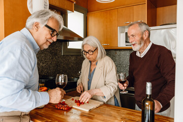 A woman is slicing tomatoes and standing at a table next to two male friends who are holding...
