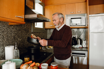 A man prepares and mixes food in a pan