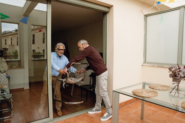 Two male friends carry a chair from one room to another while one of them smiles