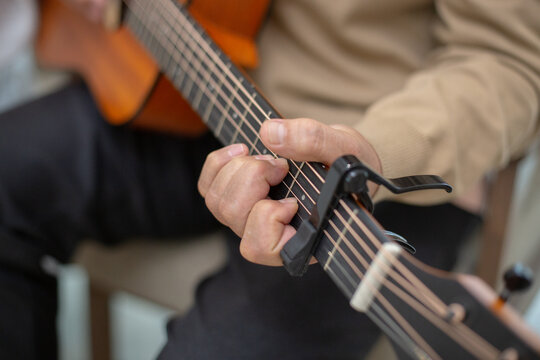 Close-up of an elderly man hand playing acoustic guitar using a capo, showing detailed finger placement and chord technique. Concept of music therapy, relaxation, and senior hobbies.