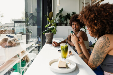 Female athlete talking to female athlete typing on phone while they sit at table