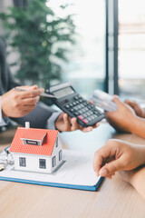 Close up of business people discussing mortgage loan with calculator, house model and contract...